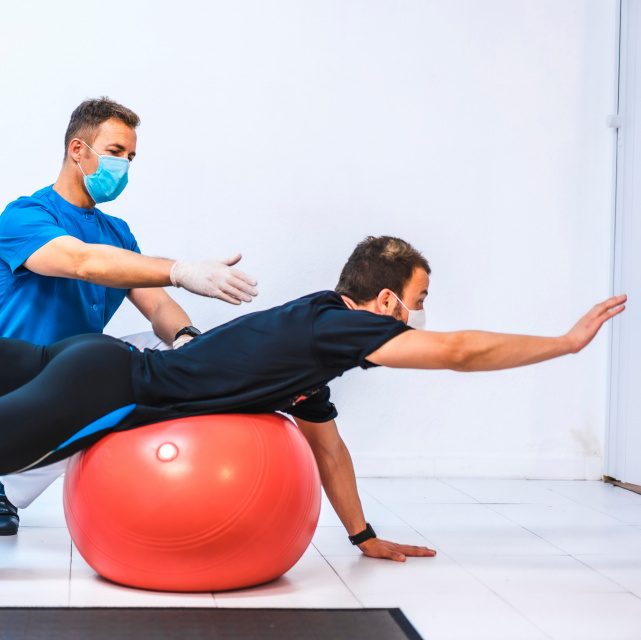 Male athlete on fit ball with male physiotherapist
