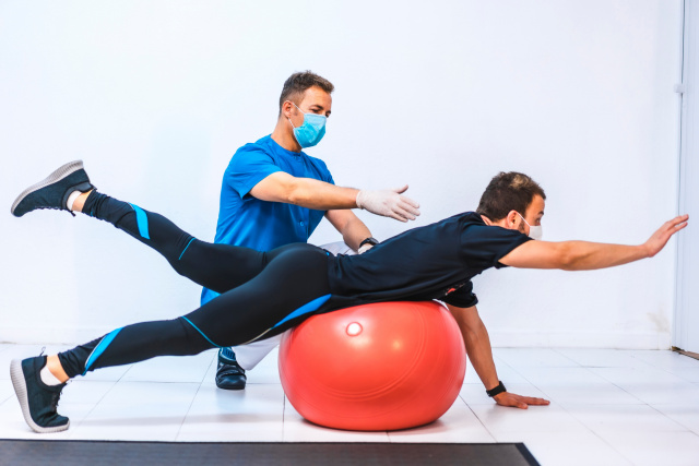 Male athlete on fit ball with male physiotherapist